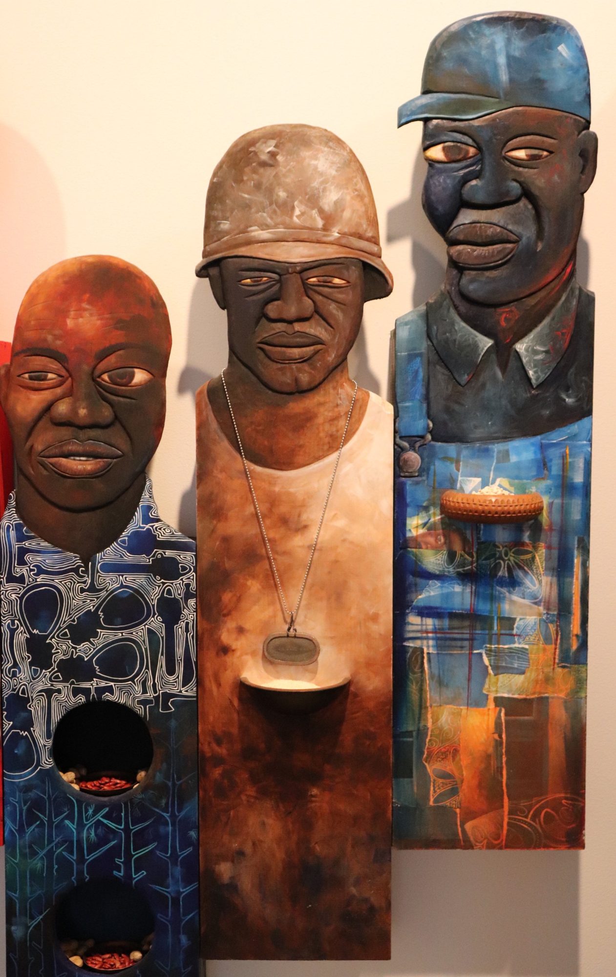 Three carved and painted wooden figures: a man in a patterned shirt, a soldier in a helmet, and a farmer in overalls